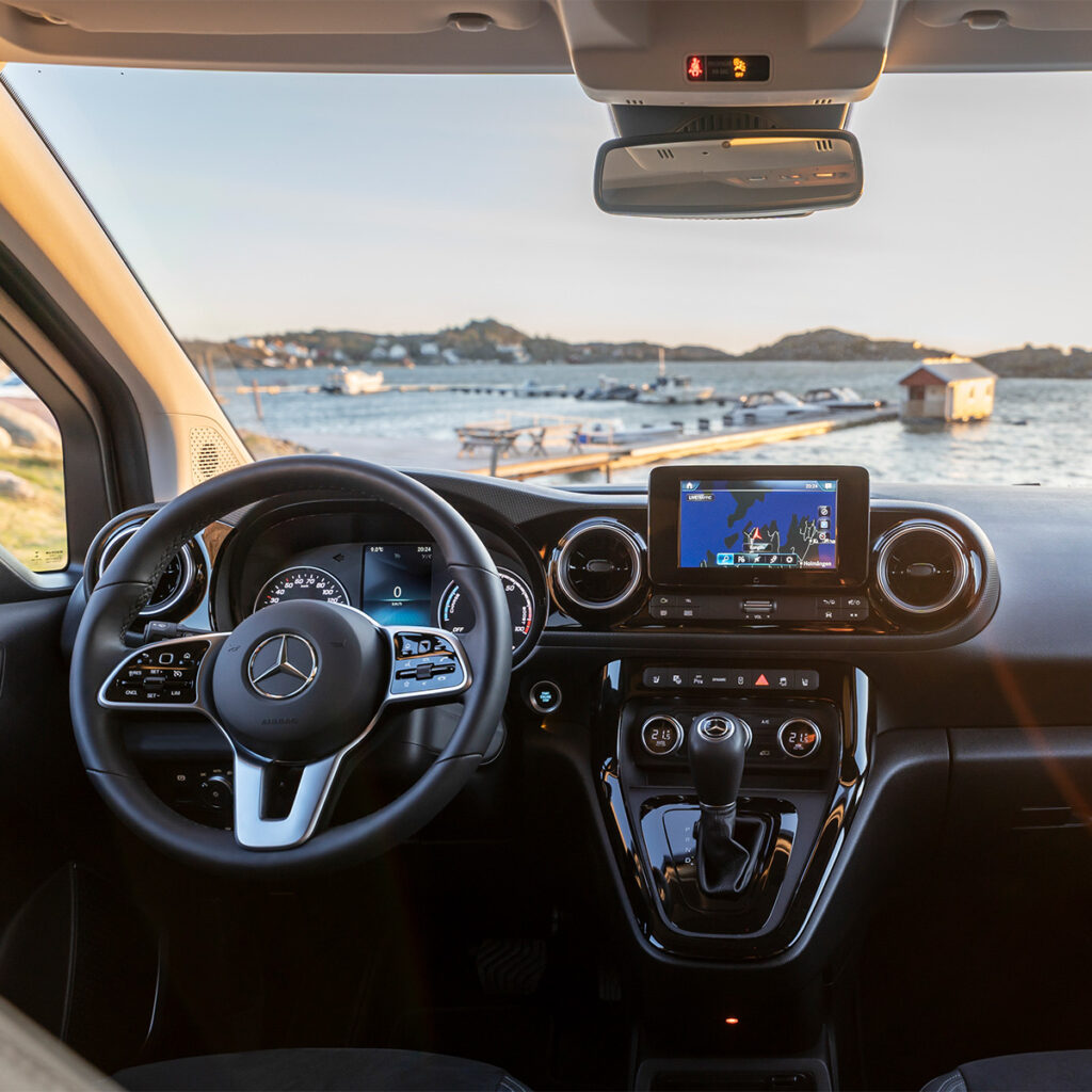 Mercedes-Benz EQT Ansicht des Cockpits mit eingeschaltetem Display. Im Hintergrund durch die Winschutzscheibe sieht man einen kleinen Jachthafen.
