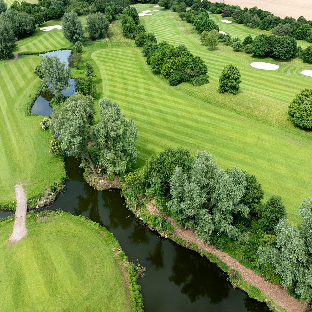 Ein weiteres Luftbild eines Golfplatzes mit klar definierten Fairways und kleinen Teichen, die die Bahnen säumen. Im Vordergrund steht ein Golfer auf dem Grün.