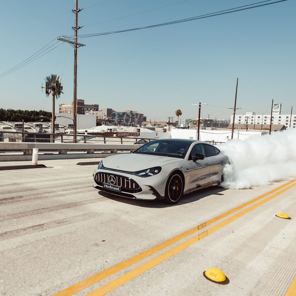 Das neue Mercedes-AMG GT 4-Türer Coupé in grau auf erner Straße mit qualmenden Reifen und Herbrand Kennzeichen